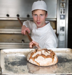 Bäcker hält einen Brotschieber mit einem Laib Brot vor einem Backofen in einer Bäckerei