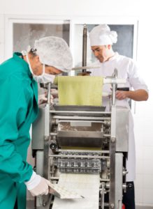 Chefs processing ravioli pasta in machine at commercial kitchen